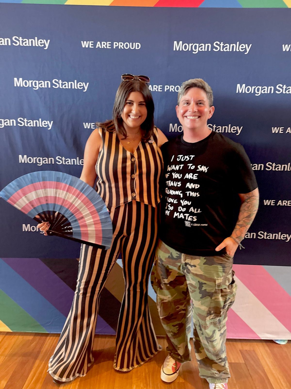 Ashley and Eli at a Pride event, Ashley holding a trans-flag fan