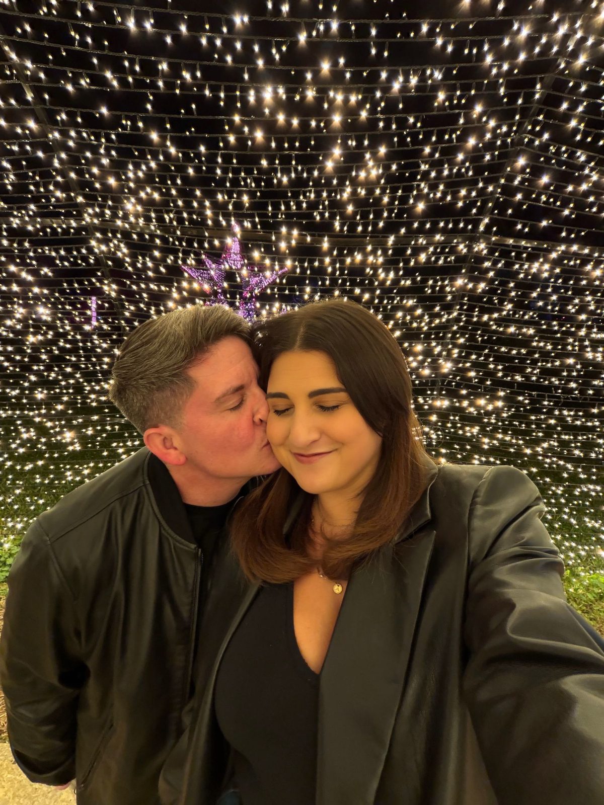 Eli kissing Ashley's cheek under string lights at night