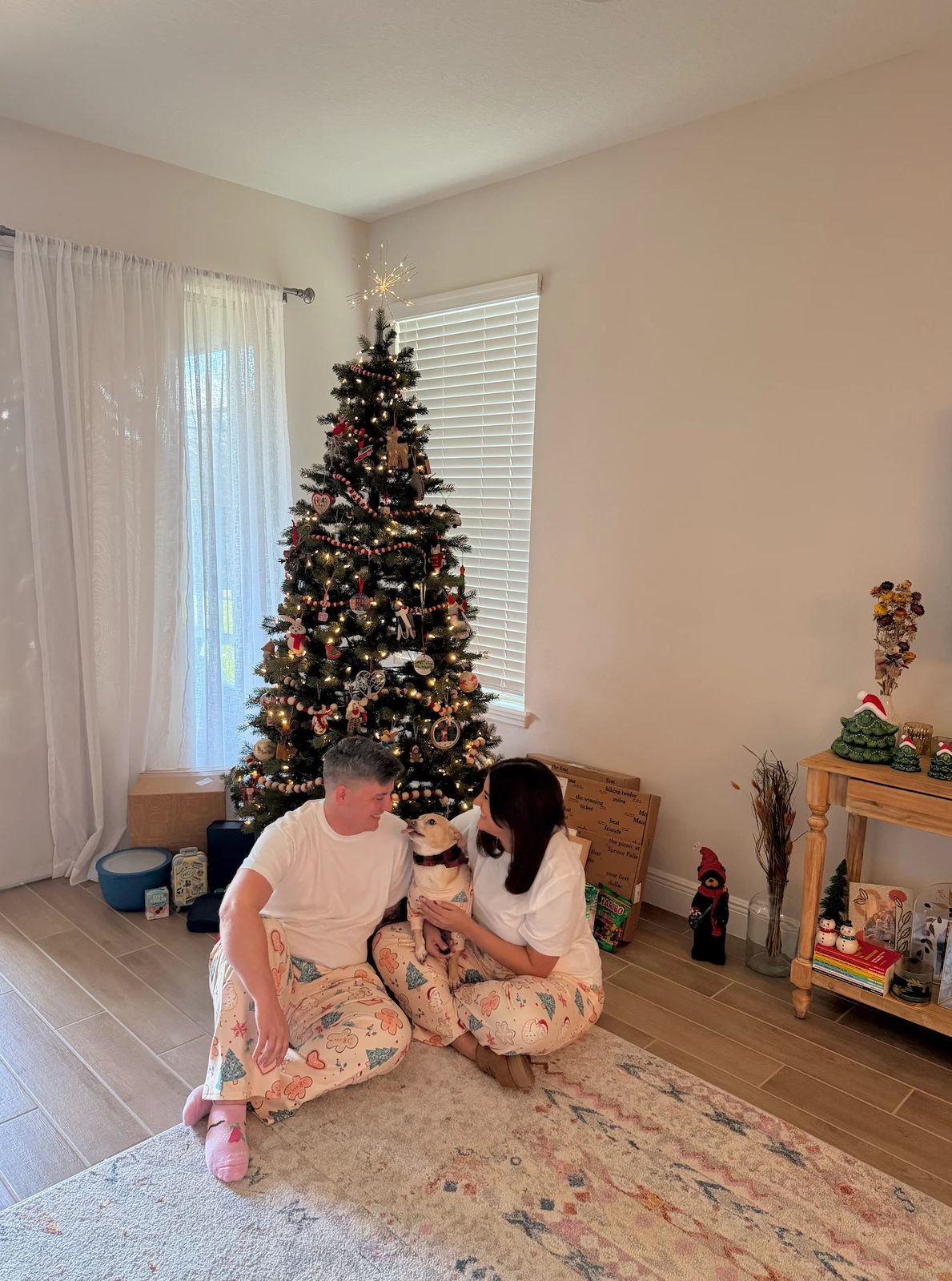 Ashley and Eli in matching pajamas by the Christmas tree with their dog