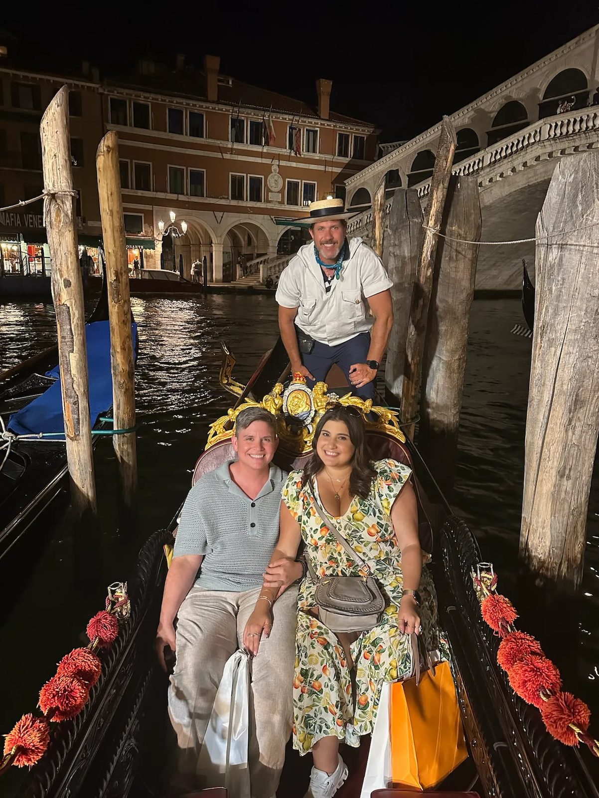 Ashley and Eli in a gondola in Venice at night, the Rialto Bridge behind them
