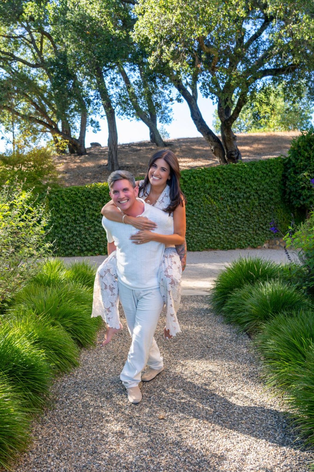 Eli giving Ashley a piggyback ride down a garden path, both laughing