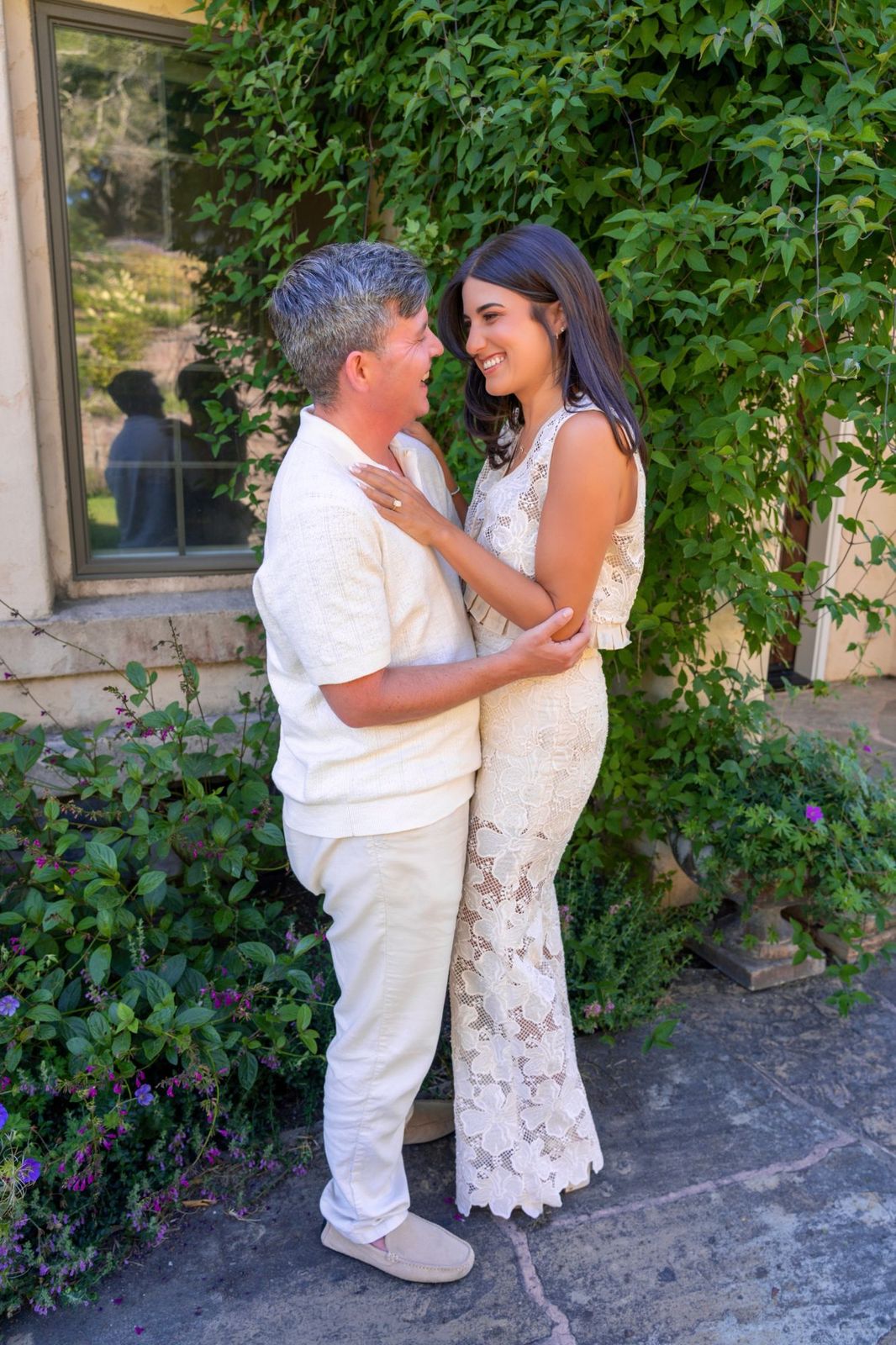 Ashley and Eli laughing together in an embrace in front of an ivy-covered wall